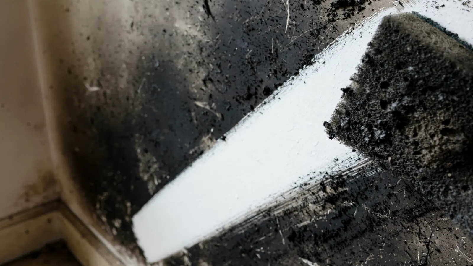 Dry chemical sponge leaving a clean stripe through soot on a white wall